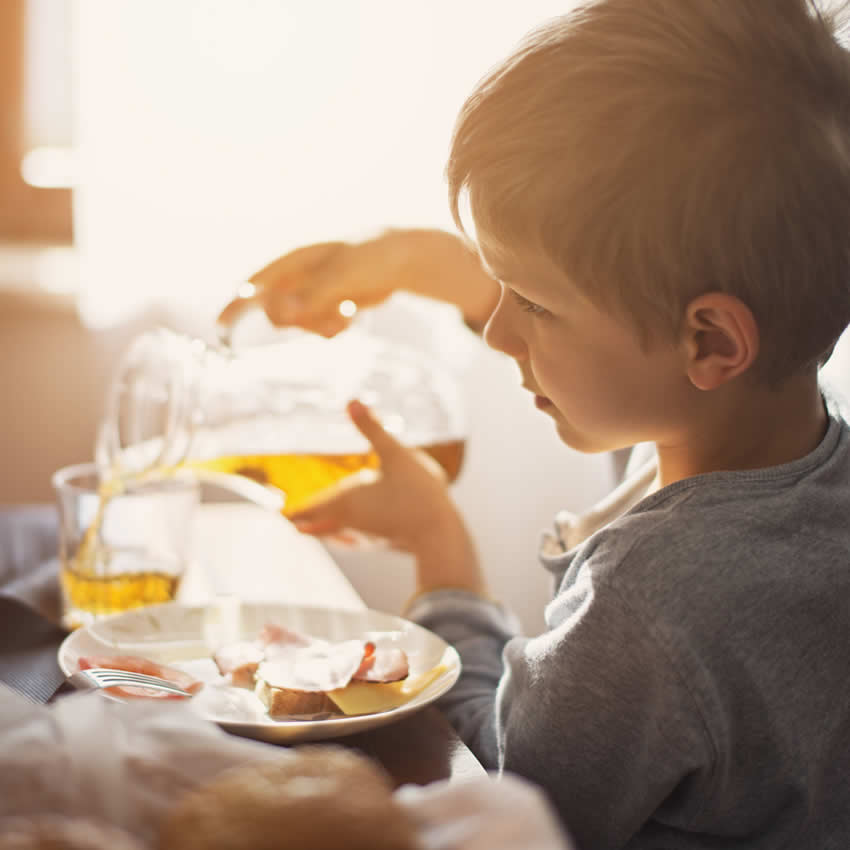 kleiner Junge gießt Apfelschorle ins Glas
